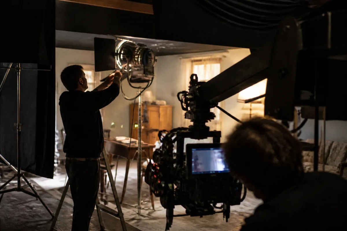 Chef opérateur ajustant un projecteur lors d’un tournage de film en studio, entouré d’équipements de cinéma